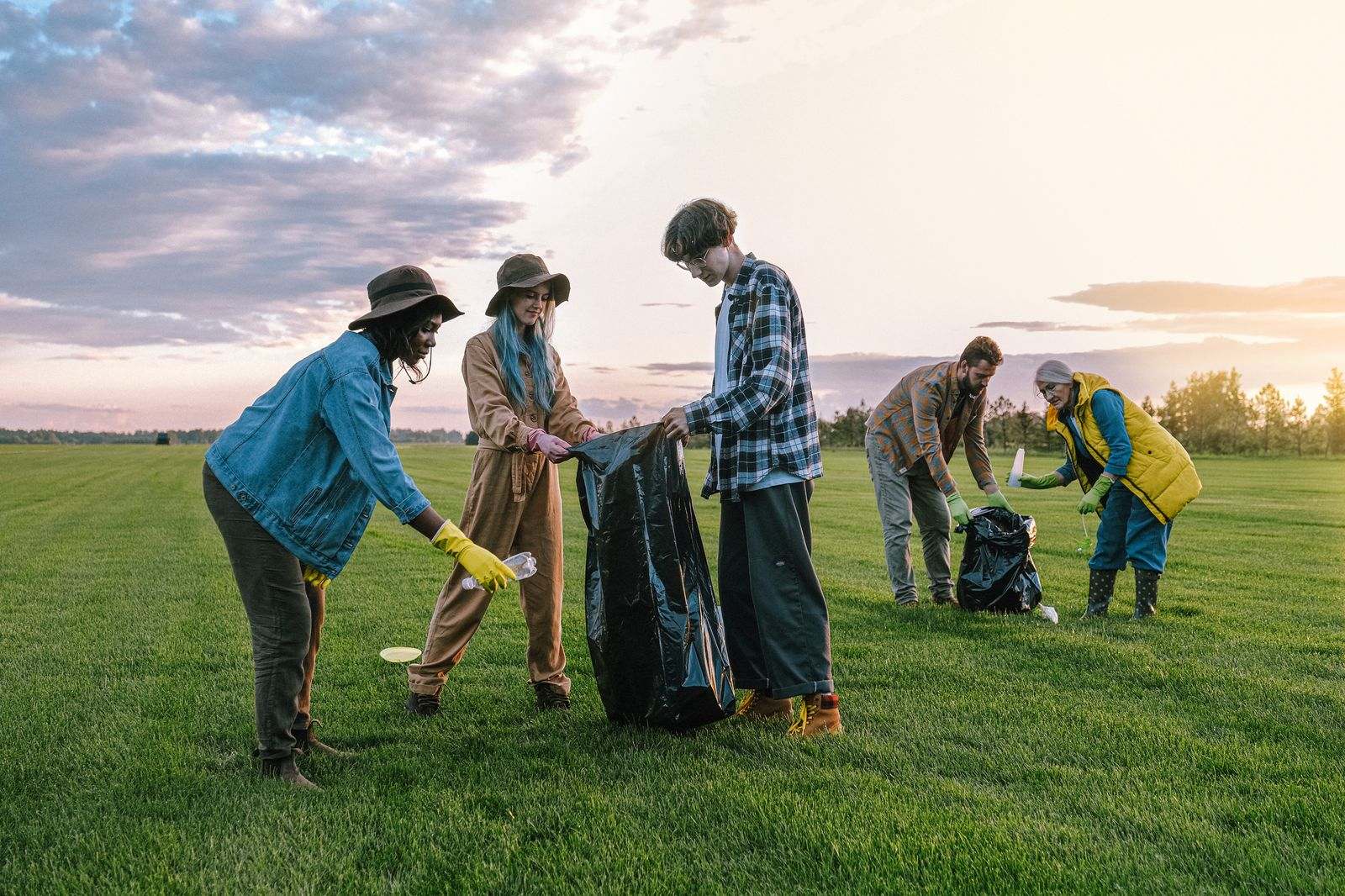 A group of volunteers picking up litter in a grassy field at sunset