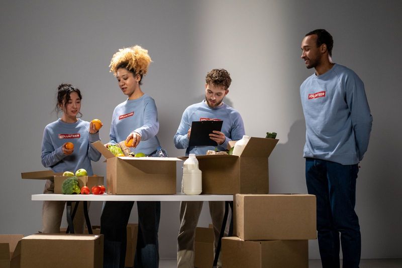 Volunteers sorting fresh produce and groceries into cardboard boxes at a table
