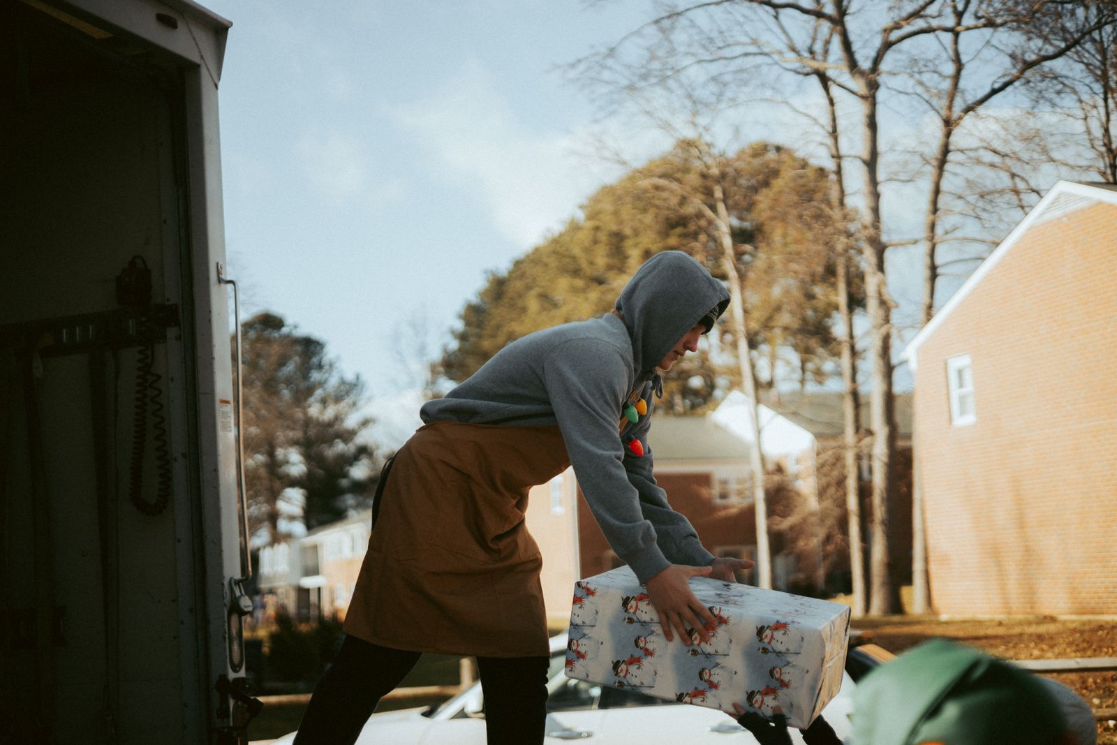 A volunteer lifting a wrapped donation box from a delivery truck on a residential street