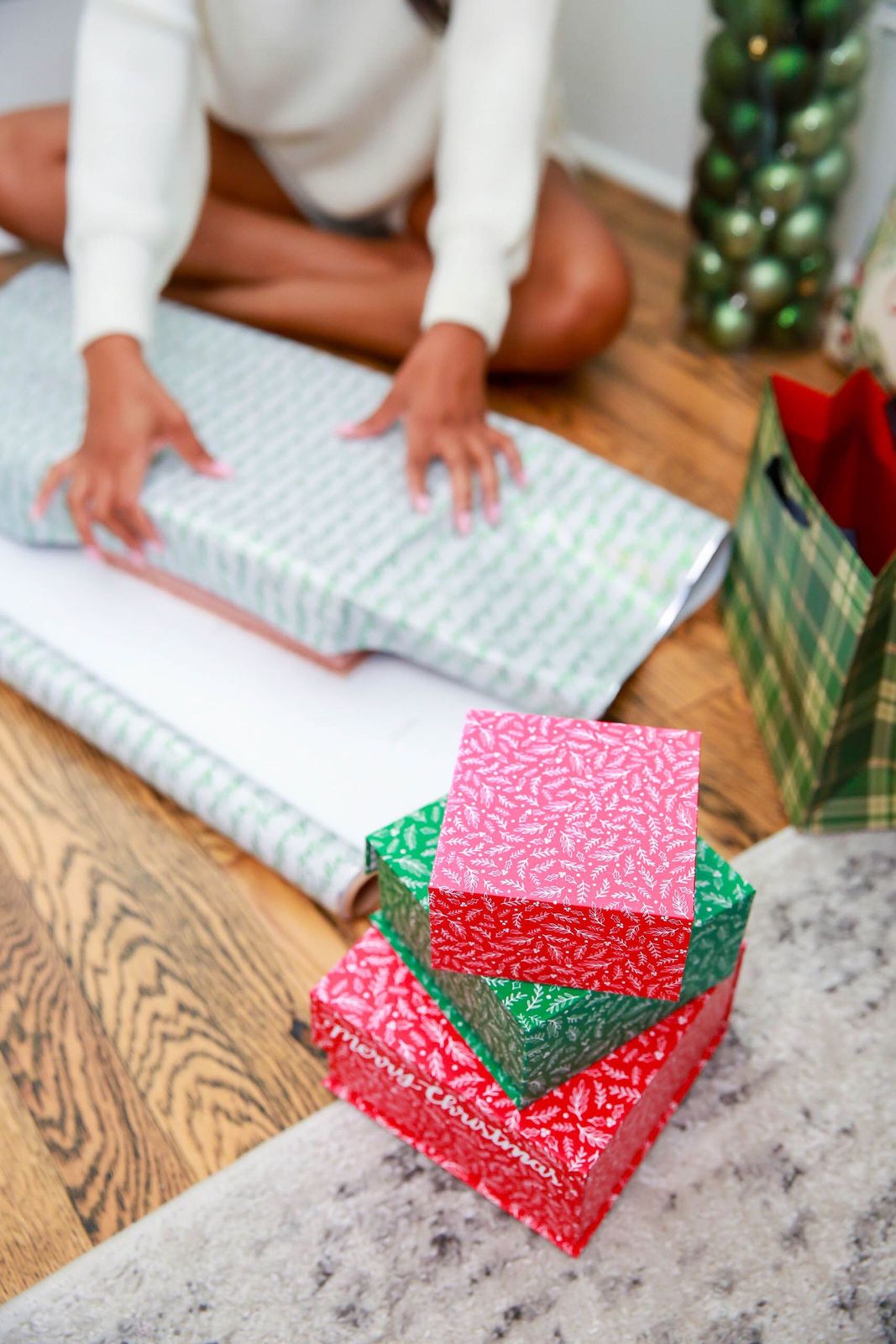 A person wrapping holiday presents in bright paper on a wood floor