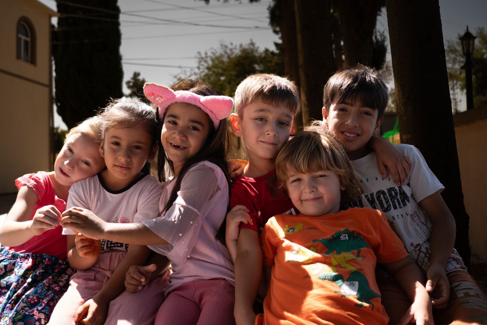 A group of smiling children sitting close together outdoors in the sun